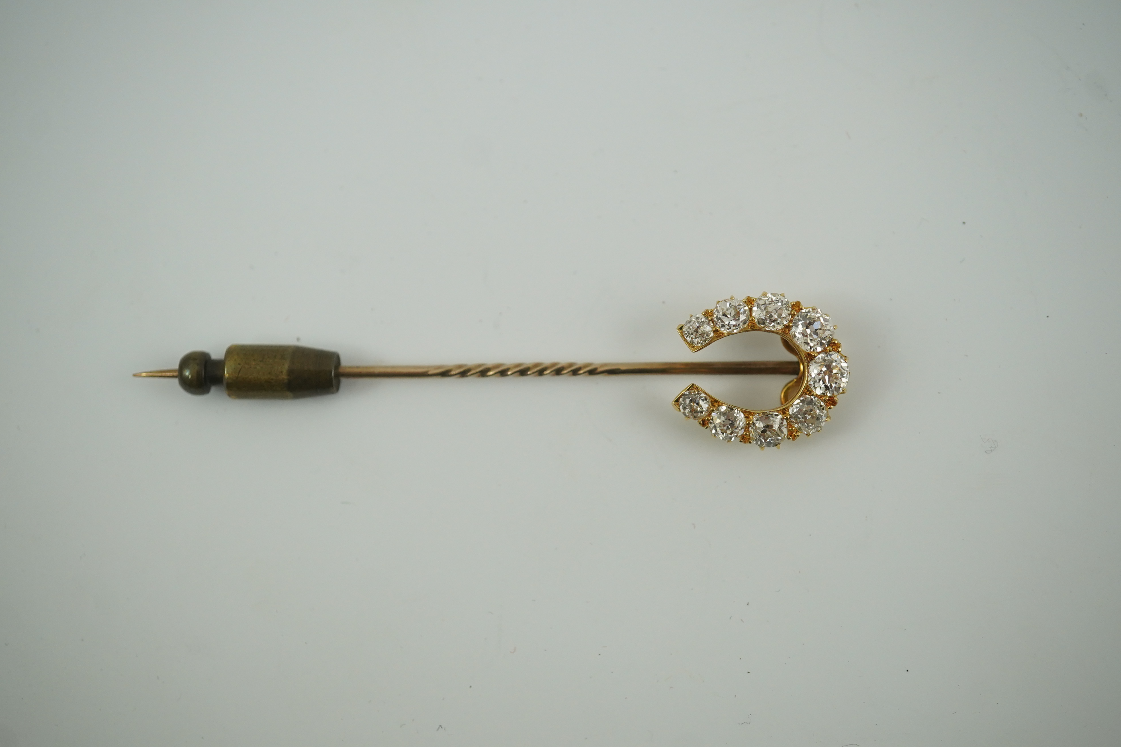 An early 20th century gold and nine stone graduated old cut diamond set horseshoe stick pin